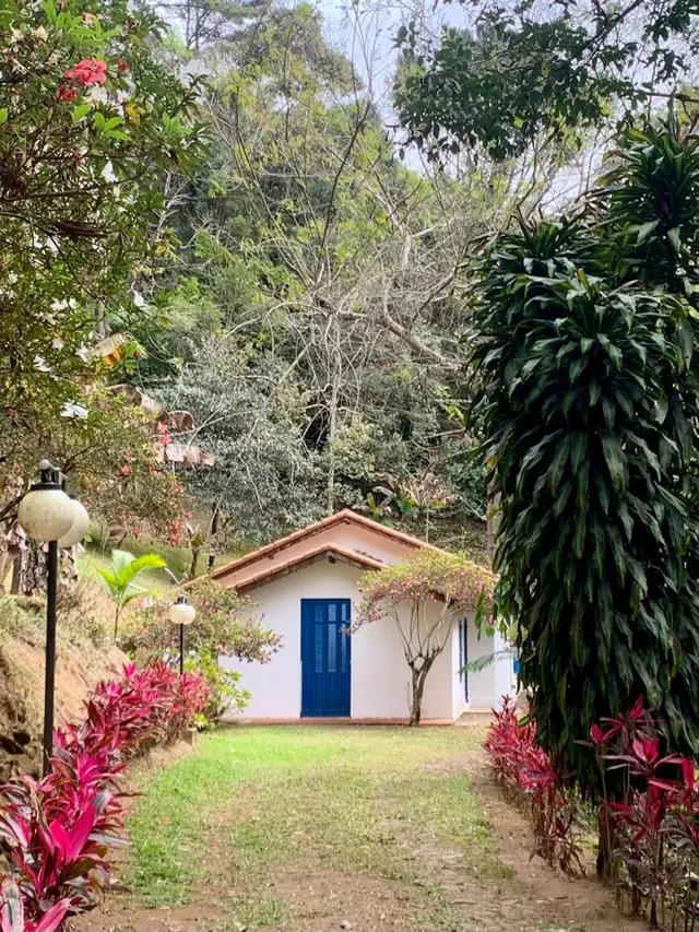 A casa-chalé, branca com portas azuis, cercada de jardim